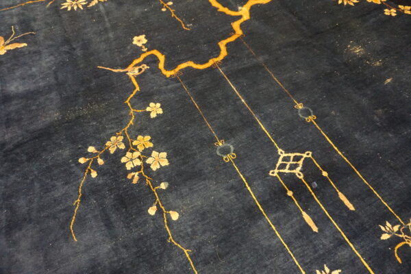 Deep blue rug surface displays a gold and beige pattern of flowering branches, a small bird, and hanging tassels.