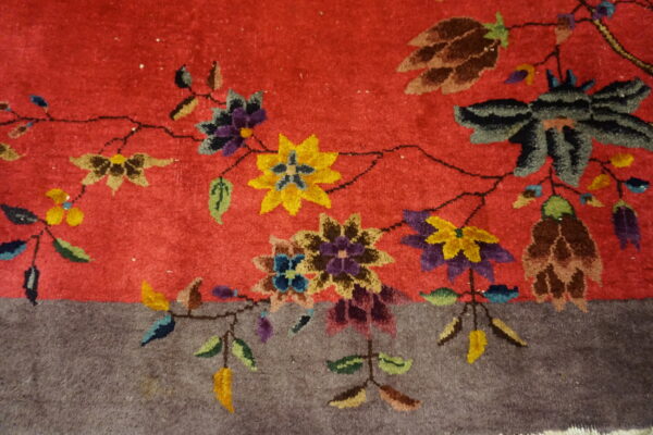 A brightly colored floral vine pattern separates the red rug field from the solid textured gray border.