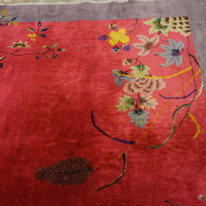 Textured red rug with multicolored botanical designs and a wide dusty purple border on wooden flooring.