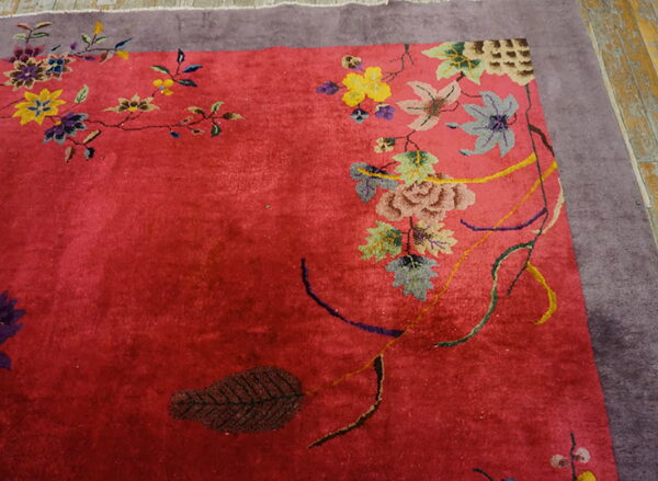 Textured red rug with multicolored botanical designs and a wide dusty purple border on wooden flooring.