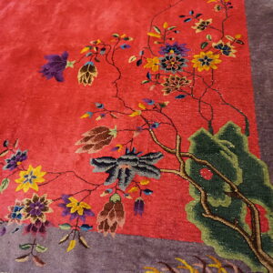 Vivid red rug featuring a detailed design of flowering branches and green scenery next to a purple border.