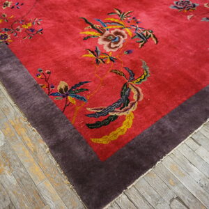 Deep red rug with lush multicolored floral motifs and a solid dark purple border on rustic gray flooring.