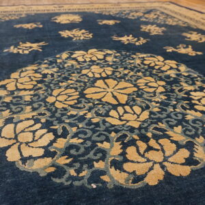 Close view of a dark blue rug featuring a tan floral medallion and scattered motifs on wood flooring.