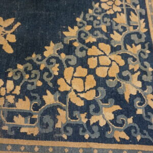 Dark blue rug corner showing golden tan flowers, teal vines, and a geometric fretwork border.