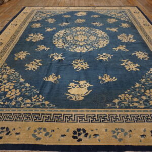 Low-pile indigo rug with tan floral motifs and a central medallion on wide wood planks.