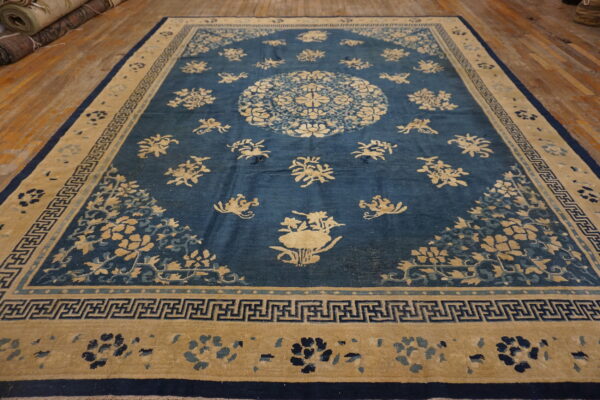 Low-pile indigo rug with tan floral motifs and a central medallion on wide wood planks.