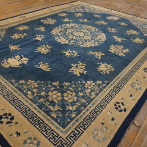Deep blue rug with tan scattered floral motifs and geometric borders laid on light brown wooden floorboards.