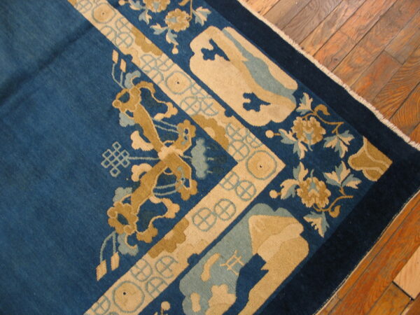 Deep blue rug corner with thick tan and pale blue stylized floral patterns visible on hardwood floor.