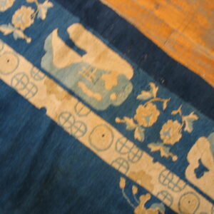 Blue rug with broad beige borders featuring floral and wheel patterns on warm-toned wood planks.