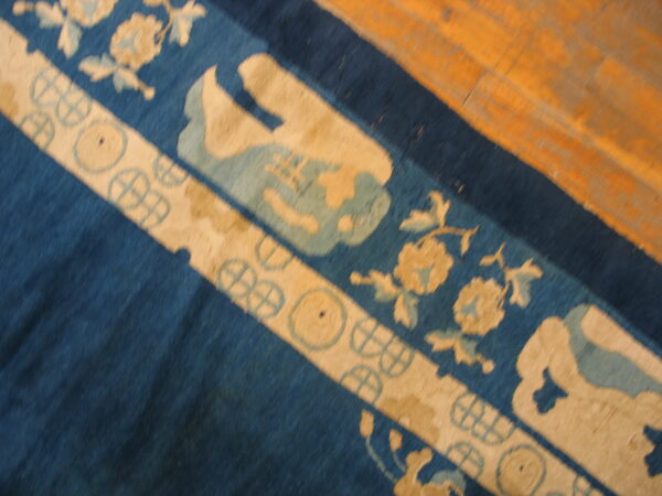 Blue rug with broad beige borders featuring floral and wheel patterns on warm-toned wood planks.