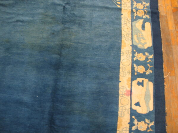 Mottled blue rug field beside a border featuring cream floral and abstract patterns on wood planks.