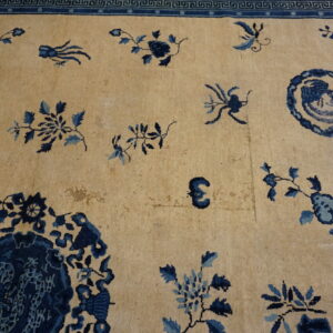 Low-pile beige rug features scattered indigo and light blue botanical motifs with an ornate blue fret border.