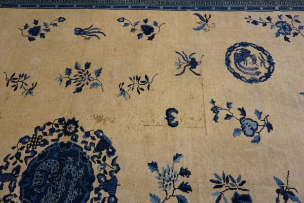 Low-pile beige rug features scattered indigo and light blue botanical motifs with an ornate blue fret border.