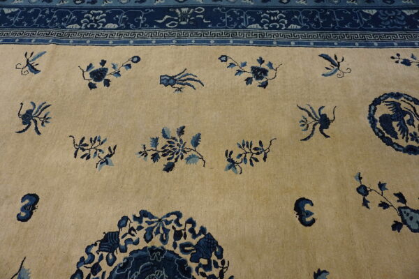 Beige rug with scattered blue floral motifs and a complex dark blue ornamental border.