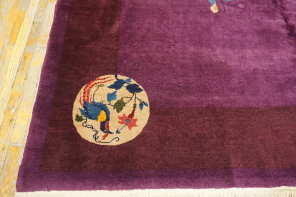 Magenta rug with a maroon border corner featuring a colorful bird medallion on distressed yellow wood.