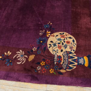 Deep purple rug with vase and floral motifs bordering the corner rests on light wood plank flooring.