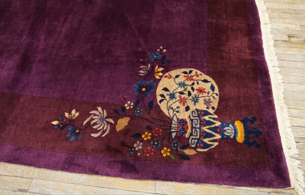 Deep purple rug with vase and floral motifs bordering the corner rests on light wood plank flooring.