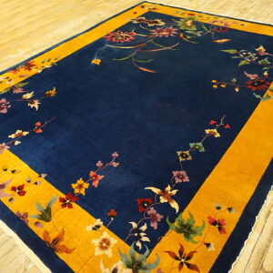 Rectangular blue and gold rug with a delicate scattered floral pattern rests on light wood plank flooring.