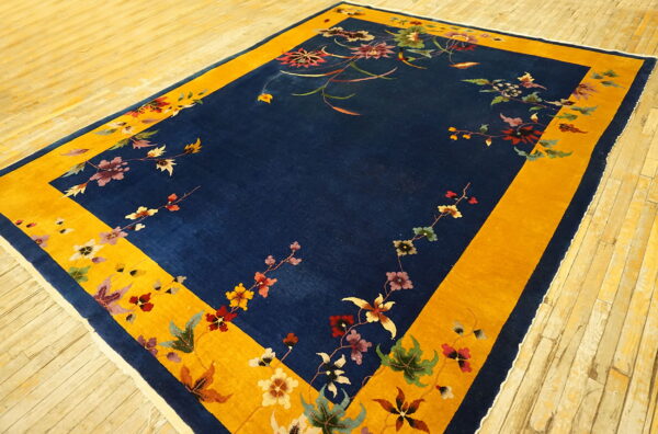 Rectangular blue and gold rug with a delicate scattered floral pattern rests on light wood plank flooring.
