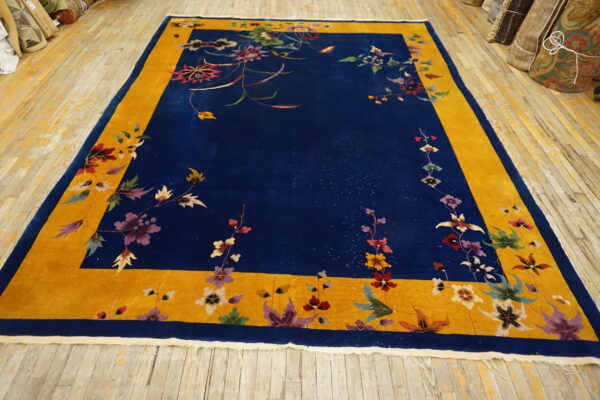 Plush deep blue rug with a wide gold border and vibrant floral patterns on wooden flooring.