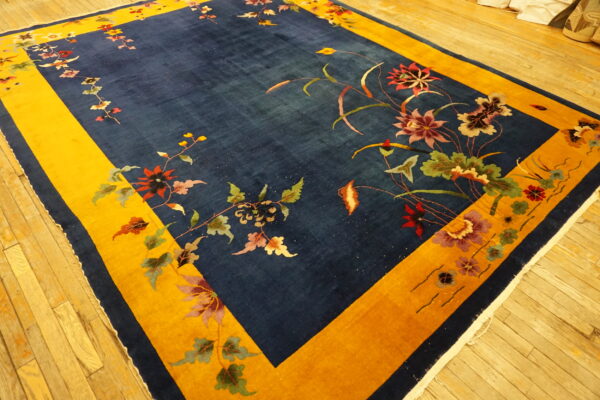 Plush indigo rug with a wide yellow frame border and scattered flowering vines on a wood floor.