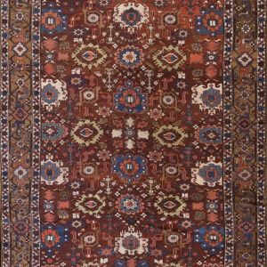 Reddish-brown rug featuring a dense geometric pattern with stylized medallions in blue, cream, and rust.