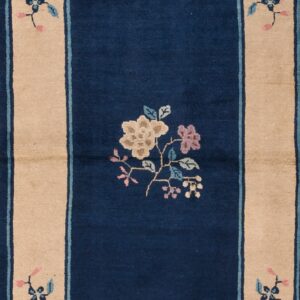 Navy blue rug with a wide beige border featuring detailed blue and pink floral patterns on wood flooring.