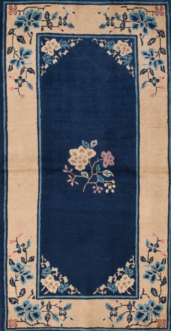 Navy blue rug with a wide beige border featuring detailed blue and pink floral patterns on wood flooring.