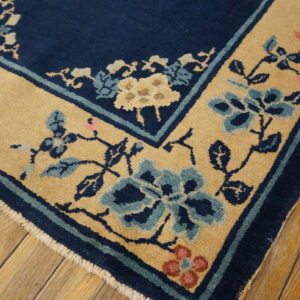 A navy rug with a tan floral border featuring blue and pink accents rests on distressed wooden floorboards.