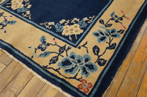 A navy rug with a tan floral border featuring blue and pink accents rests on distressed wooden floorboards.