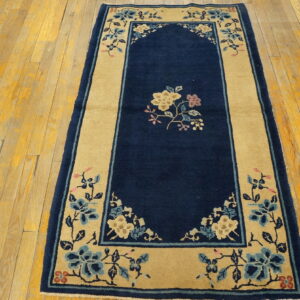 Navy blue and tan rug with a floral pattern and arch detail rests on yellow hardwood planks.