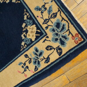 Navy rug with a gold floral border, featuring blue and cream accents, rests on worn wood planks.