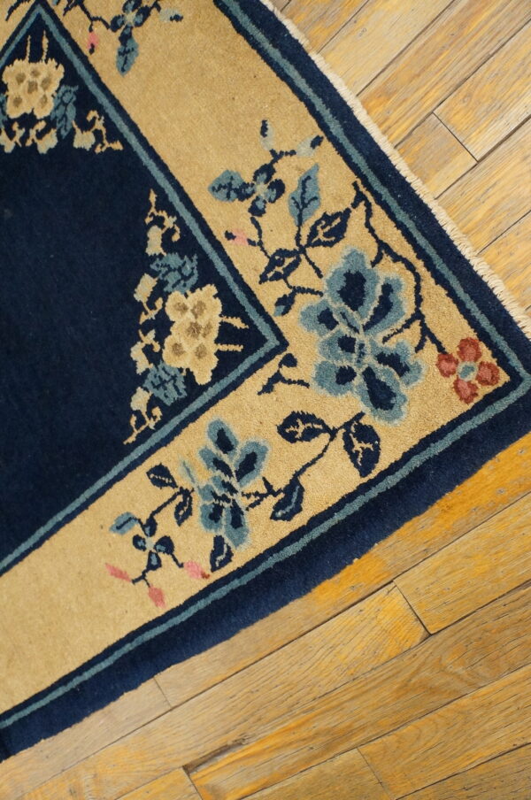 Navy rug with a gold floral border, featuring blue and cream accents, rests on worn wood planks.