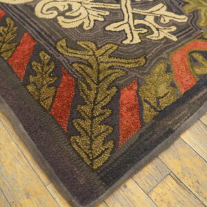 Textured rug corner in dark gray, olive, and rust floral patterns rests on distressed blonde wood flooring.