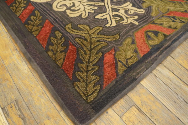 Textured rug corner in dark gray, olive, and rust floral patterns rests on distressed blonde wood flooring.