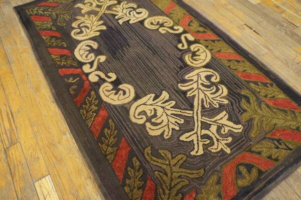 Hooked dark-toned rug featuring bold beige, red, and green stylized leaves on rustic wood plank flooring.