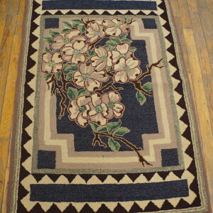 A textured navy rug with cream flowers, green leaves, and stacked geometric borders resting on wood flooring.