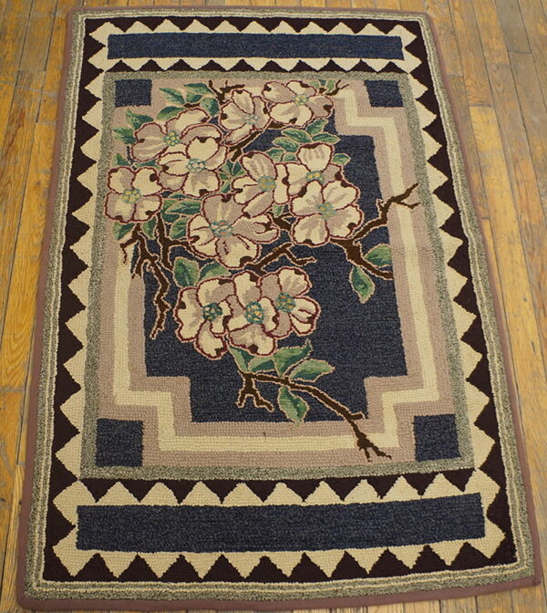 A textured navy rug with cream flowers, green leaves, and stacked geometric borders resting on wood flooring.