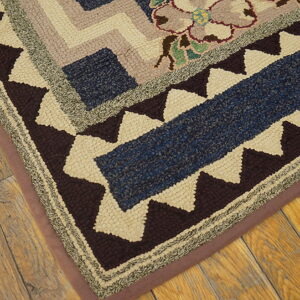 Textured hooked rug detail featuring geometric and floral patterns in blue, brown, cream, and mauve on rustic wood flooring.
