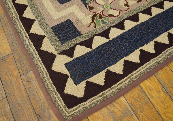 Textured hooked rug detail featuring geometric and floral patterns in blue, brown, cream, and mauve on rustic wood flooring.