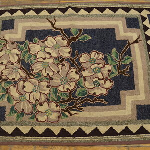Hooked rug showing beige flowers on navy blue, framed by multi-colored zigzag geometric borders.