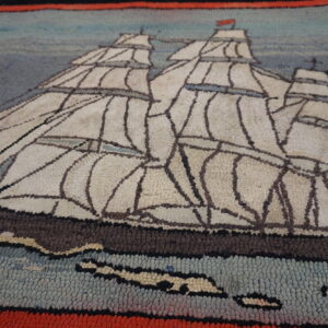Textured loop pile rug depicting a white sailing ship scene against blue and gray, bordered in red and black.