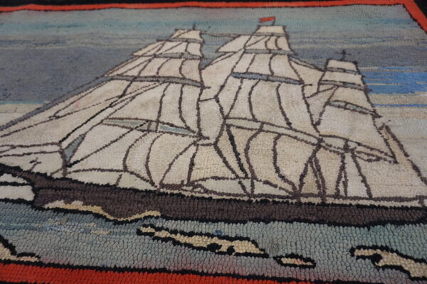 Textured loop pile rug depicting a white sailing ship scene against blue and gray, bordered in red and black.