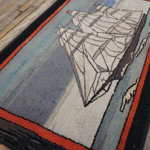 A low-pile blue and cream rug with a ship motif and red border rests on worn wooden planks.