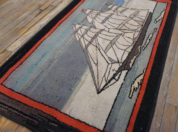 A low-pile blue and cream rug with a ship motif and red border rests on worn wooden planks.