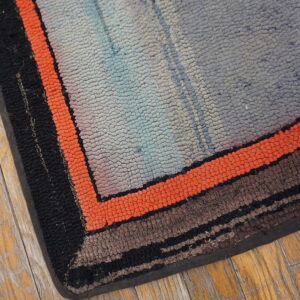 Textured rug corner with orange, black, and gray stripes rests on distressed wooden floorboards.