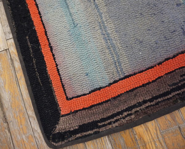 Textured rug corner with orange, black, and gray stripes rests on distressed wooden floorboards.