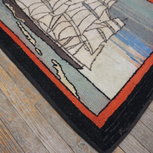Cream, blue, and gray sailboat rug with black and orange borders on weathered wood plank flooring.