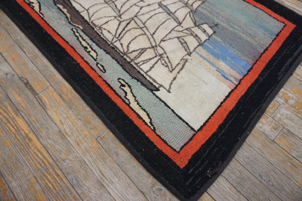 Cream, blue, and gray sailboat rug with black and orange borders on weathered wood plank flooring.