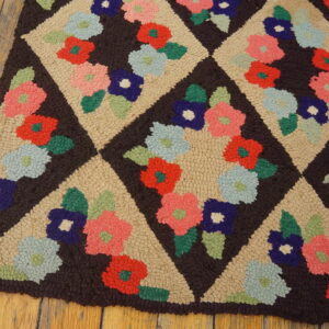 Hooked rug featuring colorful flowers in tan diamond lattices on a dark brown field, resting on wood planks.